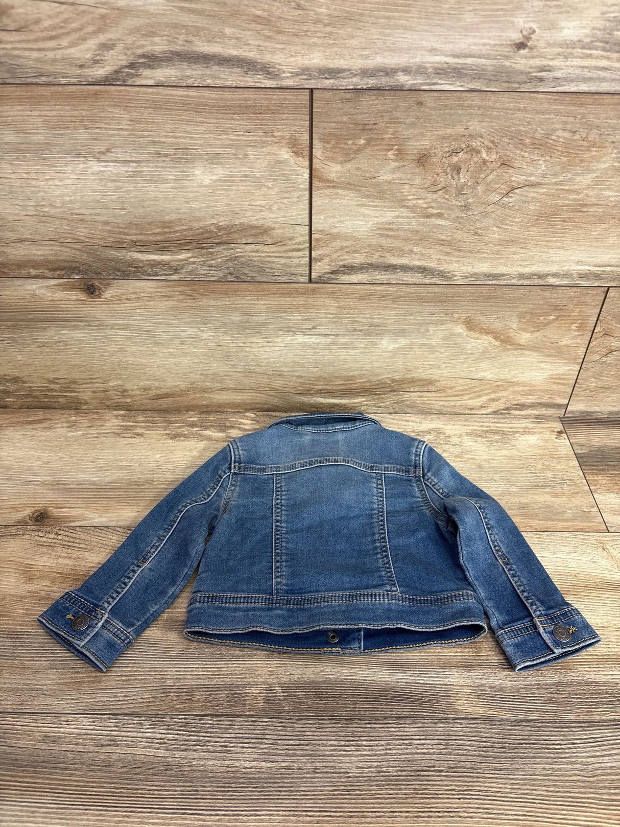 Back view of a children's blue denim jacket laid flat on wooden floor, kids resale clothing