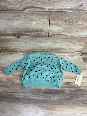 Light blue baby sweater with navy heart pattern, long sleeves, and ribbed cuffs on wooden floor background