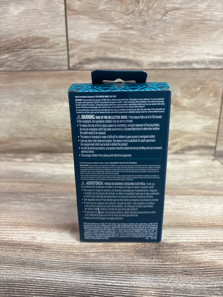 Back view of Safety 1st 36-pack plug protectors packaging showing electrical safety warnings on a wood surface