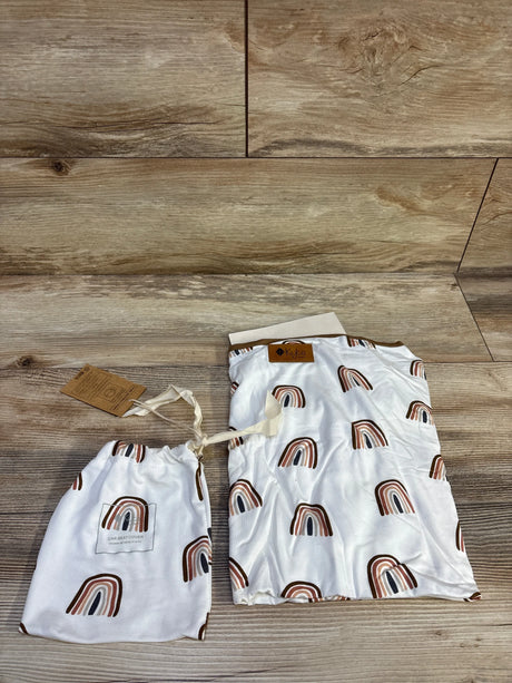 Flat lay of Kyte Baby nursing and car seat cover with rust-brown rainbow print and drawstring bag on wood background