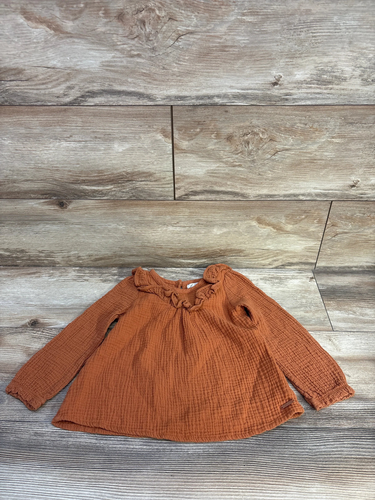 Flat lay of caramel Tahari gauze long sleeve shirt (4T) with ruffled neckline and crinkled texture on light wood background