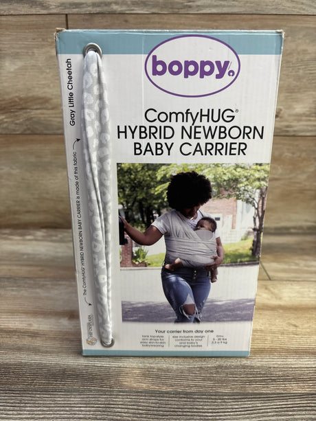 Front view of Boppy ComfyHUG Hybrid Newborn Baby Carrier packaging showcasing gray Little Cheetah fabric on a wood floor