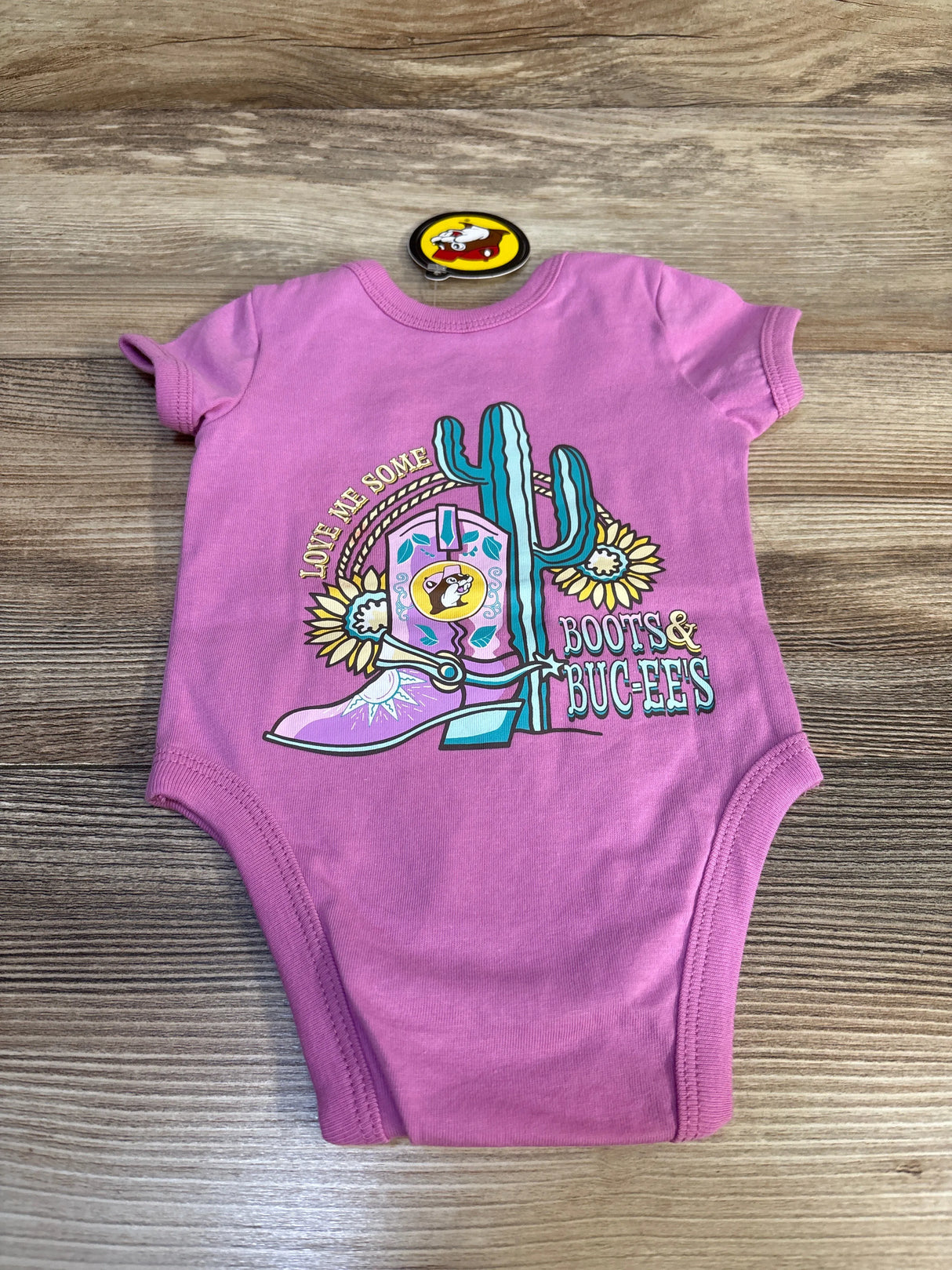 Pink baby onesie with cowboy boot, cactus, and sunflower design, 'Love Me Some Boots & Buc-Ees'