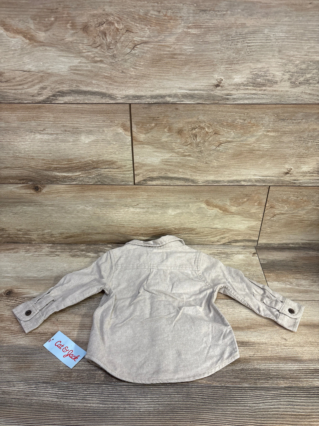 Back flat-lay of beige Cat & Jack baby button-up shirt showing cuff buttons, curved hem, and brand tag on wood background