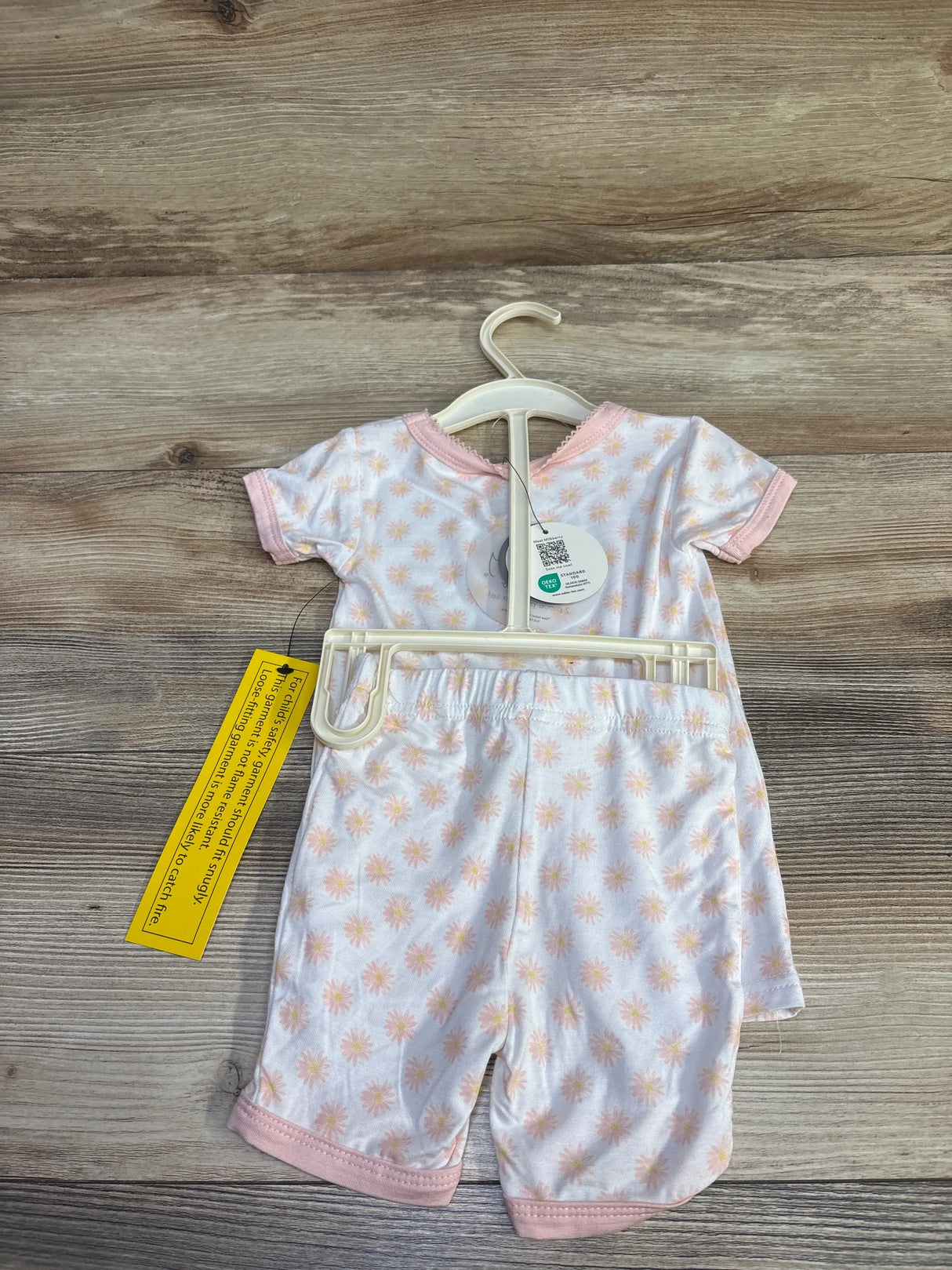 Back view of white bamboo baby pajama set with peach sunburst print and pink trim on hanger on wood floor