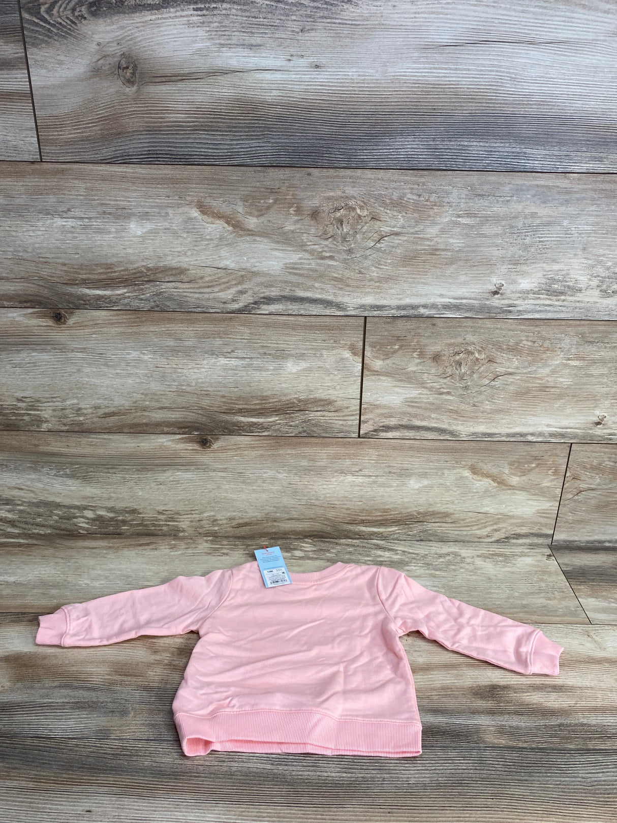 Light pink long-sleeve toddler sweater on wood plank background with price tag attached