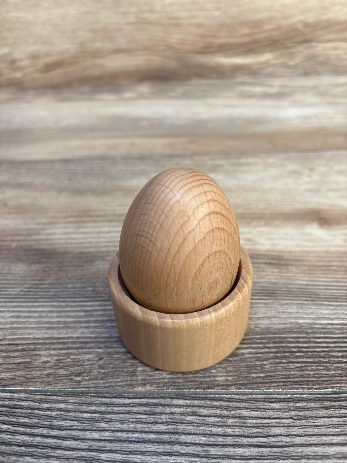 Front view of Lovevery Montessori Egg Cup showing smooth natural wood egg seated in a matching cup on a wooden tabletop