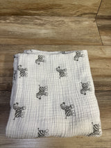 Top view of Amazing Baby muslin swaddle blanket in white with gray zebra print, laid flat on a wood floor