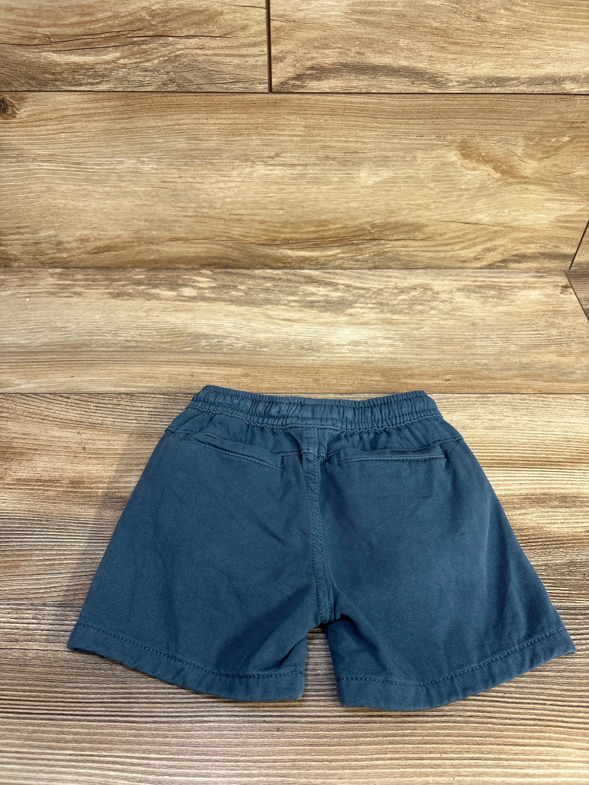 Flat-lay back view of blue Zara toddler shorts size 18 months showing elastic waistband and faux back pockets on wood background