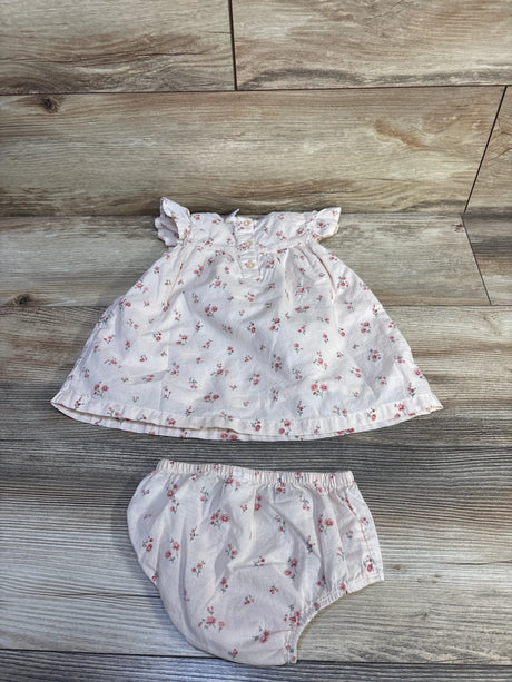 Flat lay of pink floral baby dress and matching bloomers showcasing ruffle cap sleeves, front buttons, and elastic waist on wood background