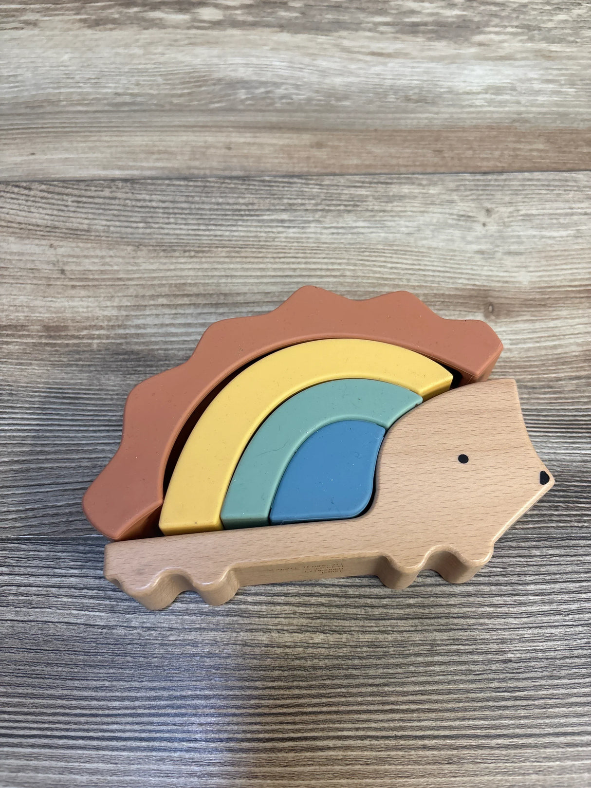 Angled view of Cloud Island silicone and wood hedgehog stacker with four pastel rainbow pieces on wood surface