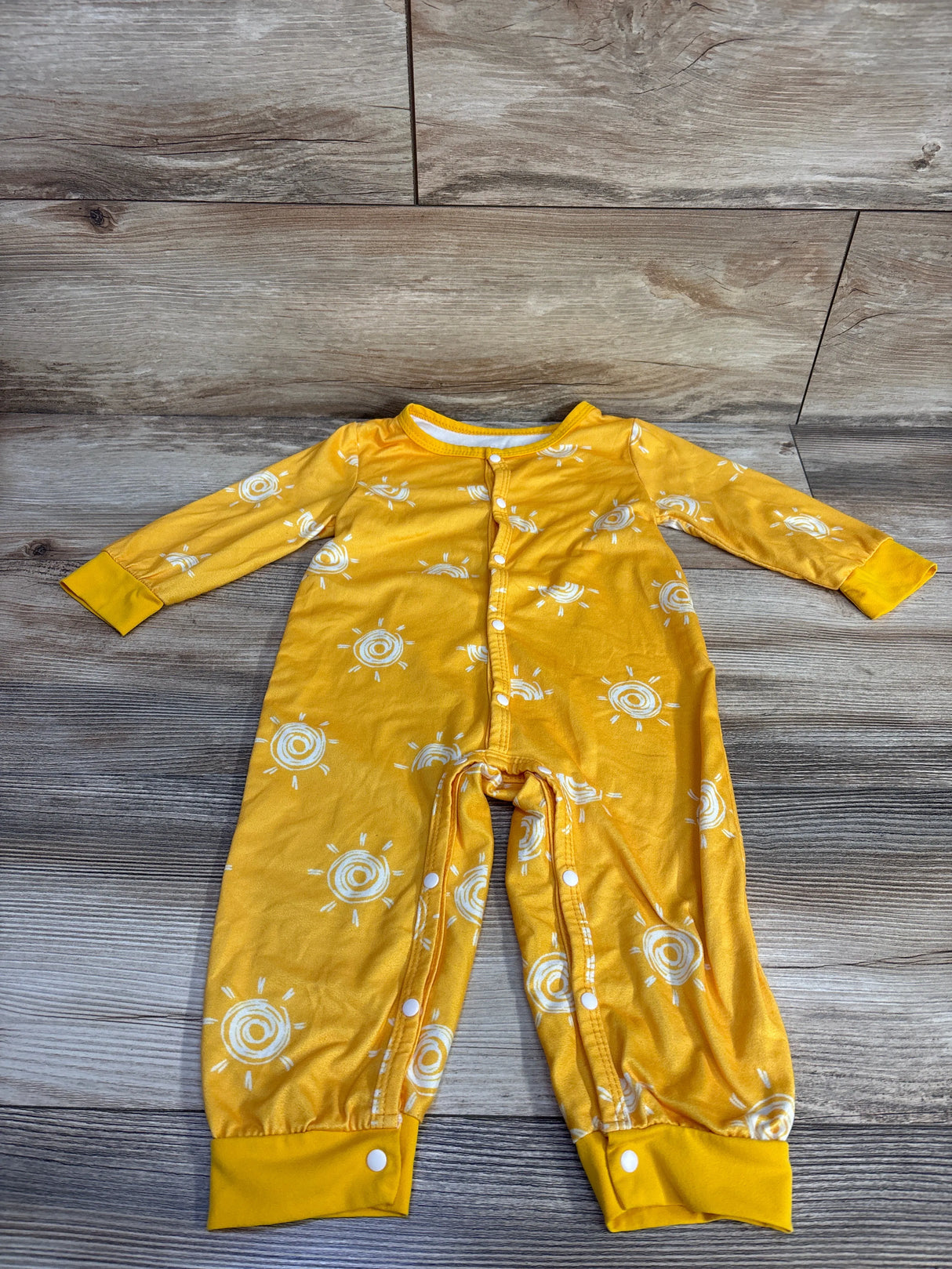Flat lay of yellow baby snap jumpsuit with white sun print showing front snap closure and fold-over cuffs on wood background