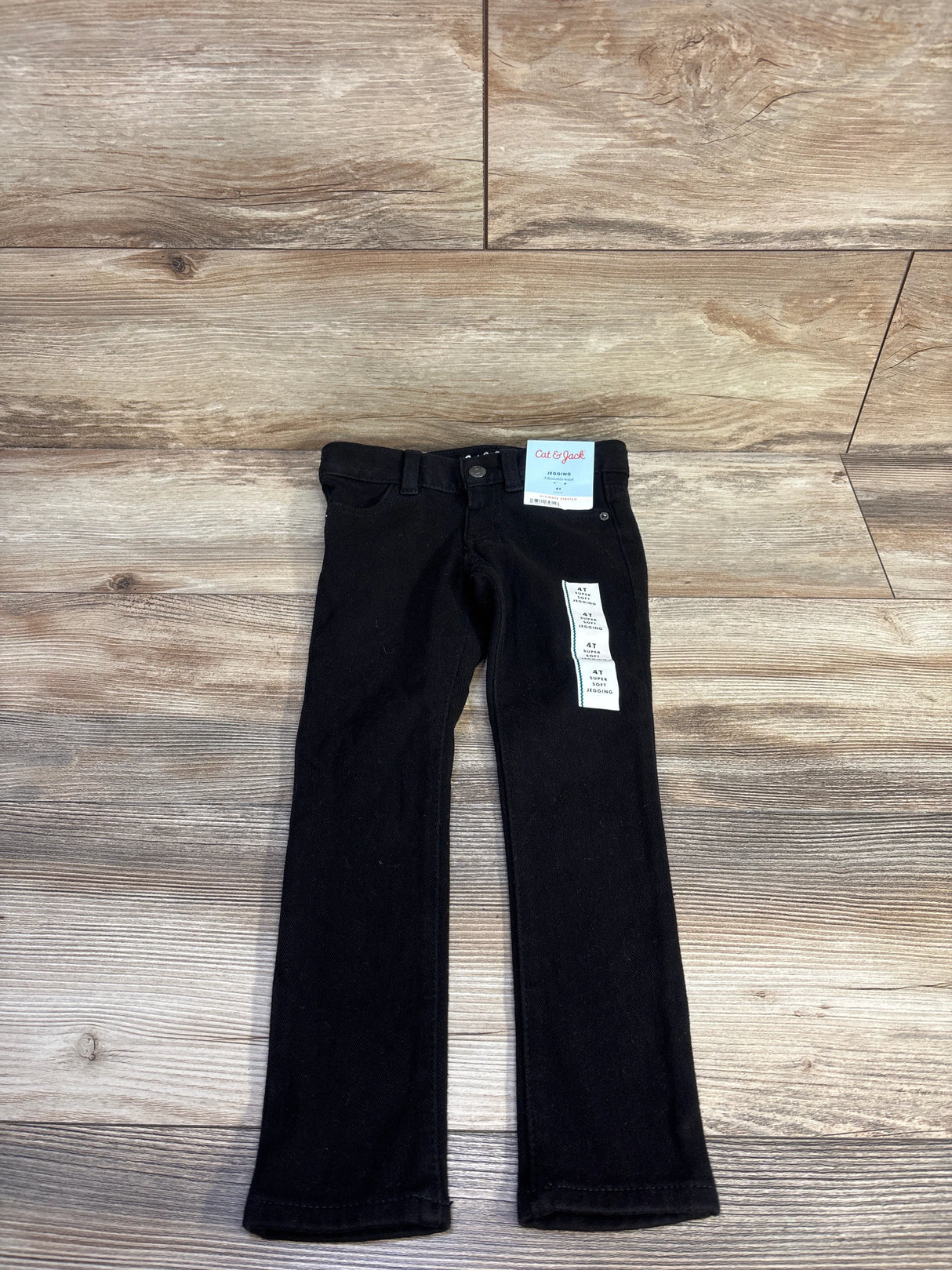 Flat lay of Cat & Jack black toddler jeggings 4T showing front button, pockets and size tags on wood floor background
