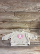 Front view of beige knit initial E sweater showcasing ribbed texture and pink heart detail on a wood background
