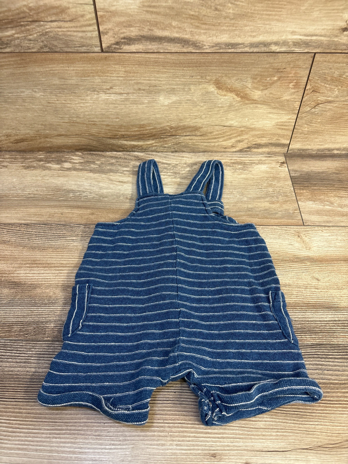 Flat lay of blue Cat & Jack striped henley shortalls, 6-9 months, showing buttoned bib and side pockets on wood floor