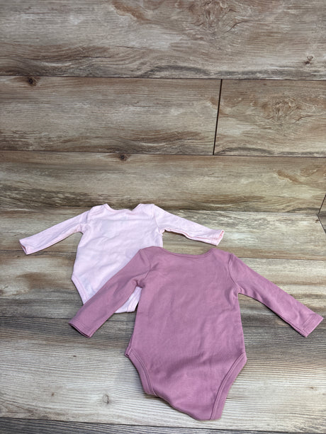 Top view of two pink long-sleeve baby bodysuits on a wood-grain background