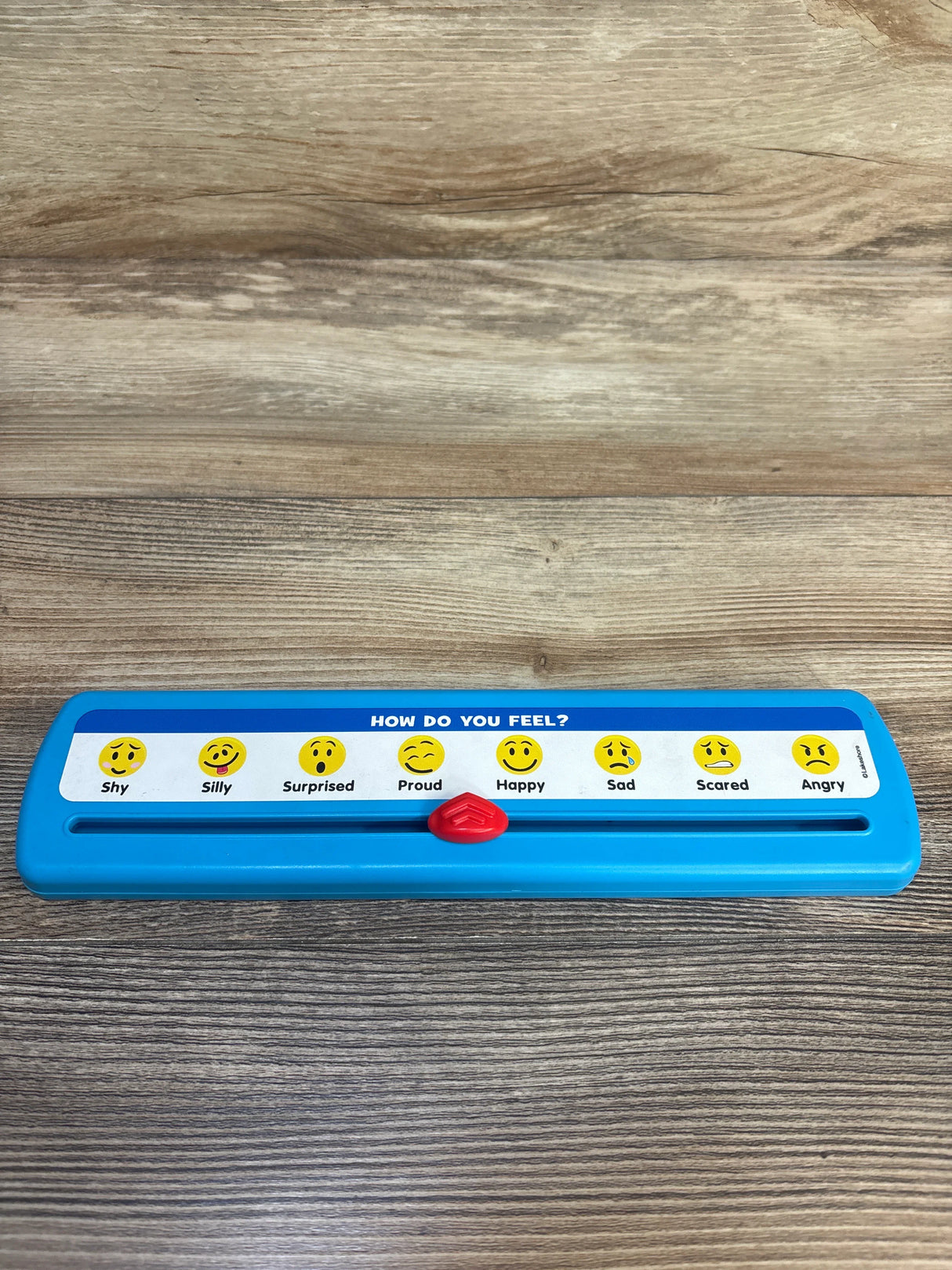 Blue children's feelings slider toy with emoji faces and emotion labels on wood surface