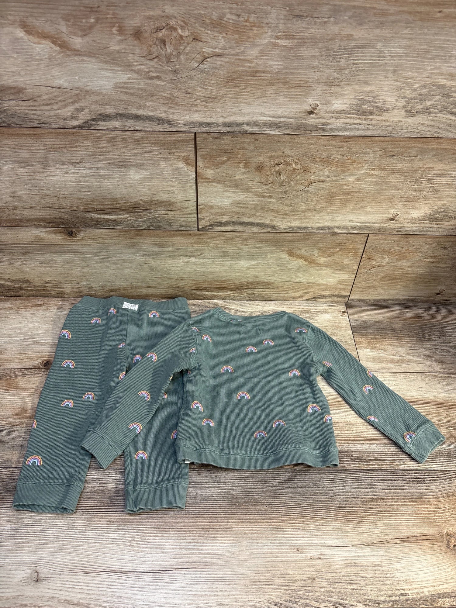 Flat lay of green waffle knit shirt and pants set showcasing rainbow print on a wood-look background
