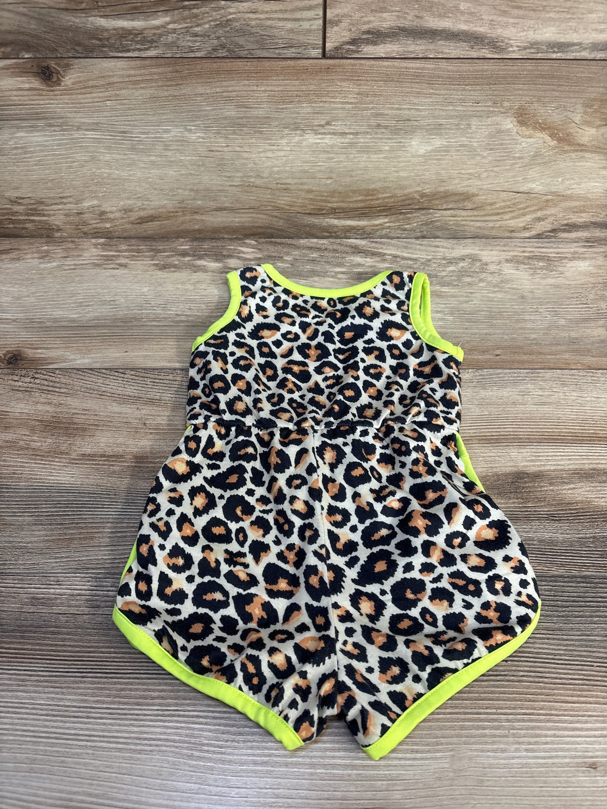 Flat-lay front of leopard tank romper showing tan-and-black print with neon yellow trim on wood floor, size 6–9M
