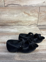 Angled view of Baby Gap black velvet Mary Jane flats showcasing front bow and adjustable strap on wood floor background