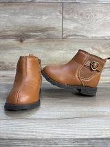 Brown toddler ankle boots with side zipper, heart buckle, and rubber soles on wood floor