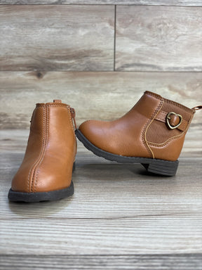 Brown toddler ankle boots with side zipper, heart buckle, and rubber soles on wood floor