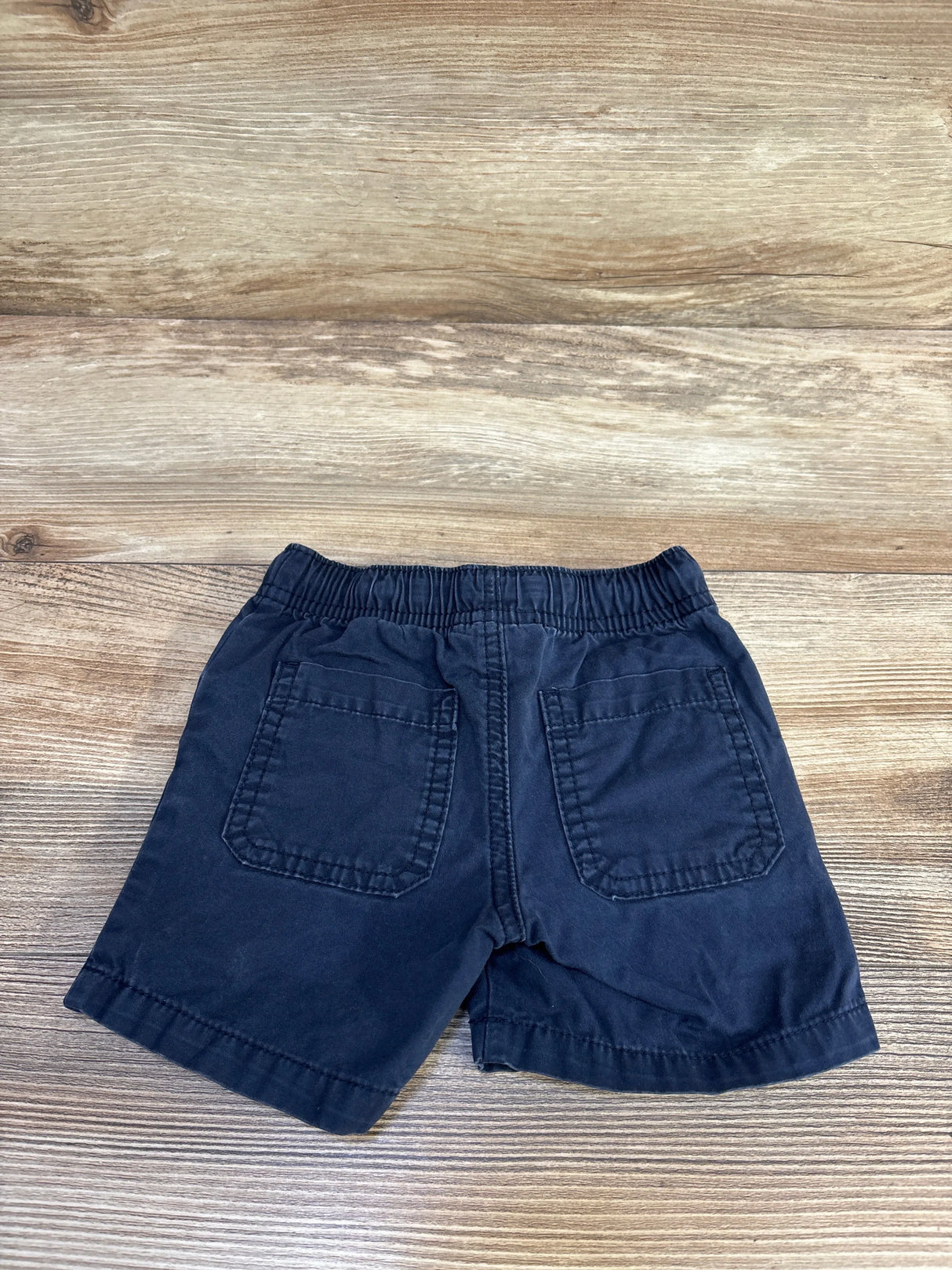 Back view of navy toddler drawstring shorts showing elastic waistband and two patch back pockets on wood background