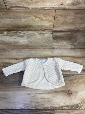 Cream knit baby cardigan with textured pattern on wood background