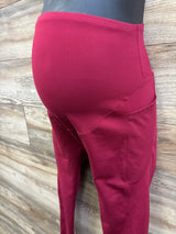 Side view of red maternity athletic leggings showing high-rise belly panel and side pockets with wood background