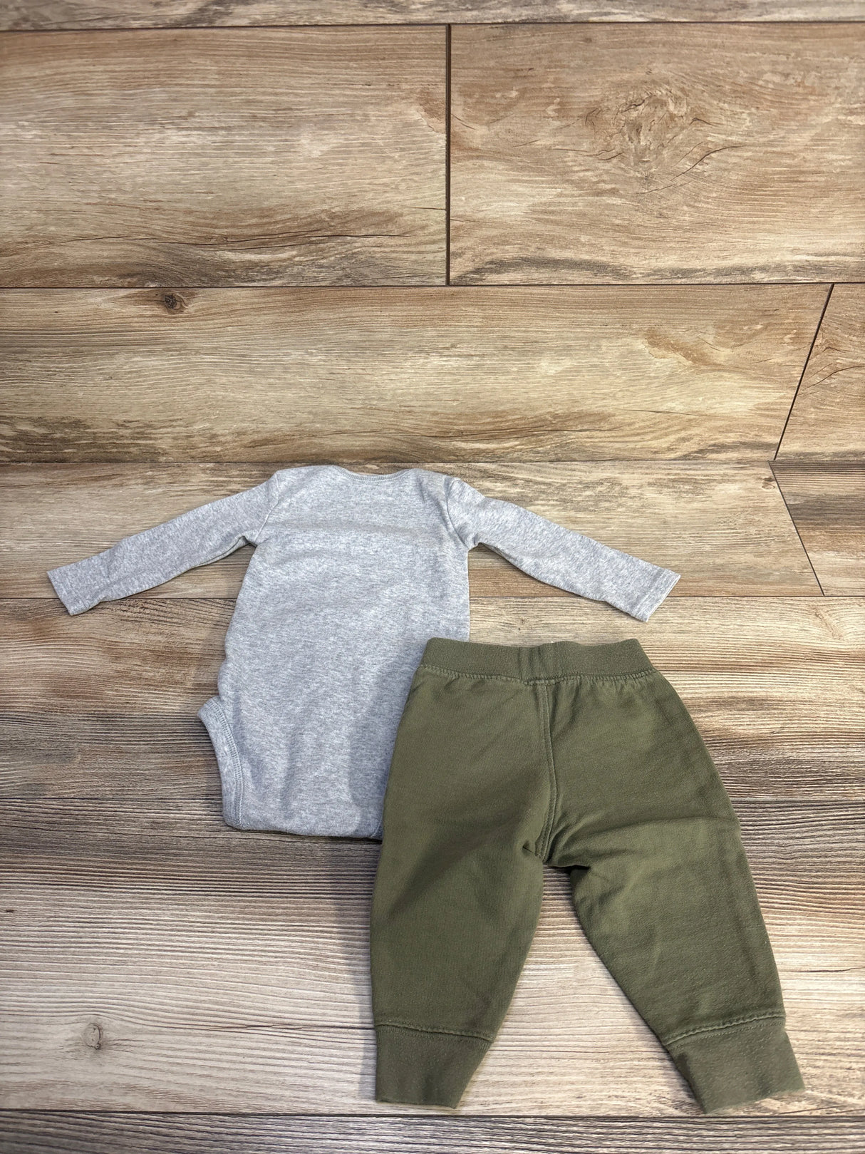 Flat-lay of baby bodysuit and pants set showing grey long-sleeve bodysuit and olive cuffed pants on wood floor