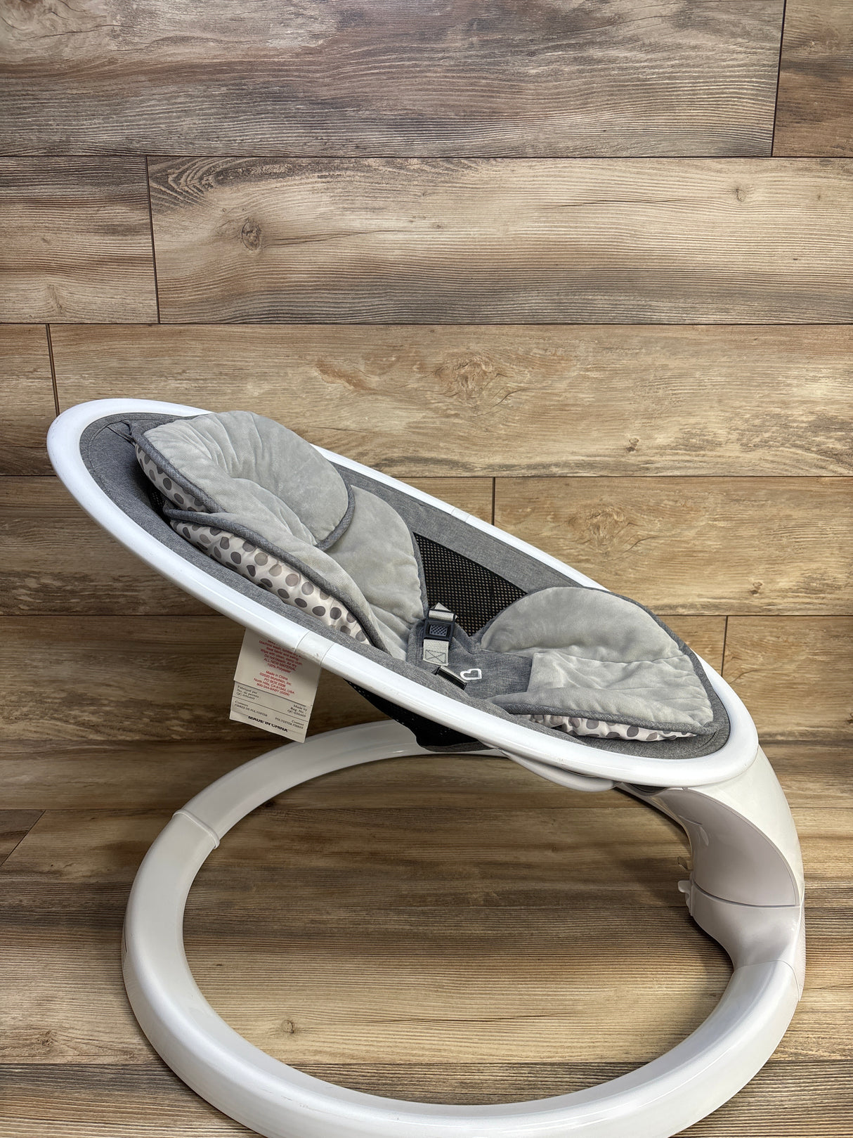 Side view of Munchkin Bluetooth-enabled baby swing with gray padded seat, harness, and white circular base on wood background