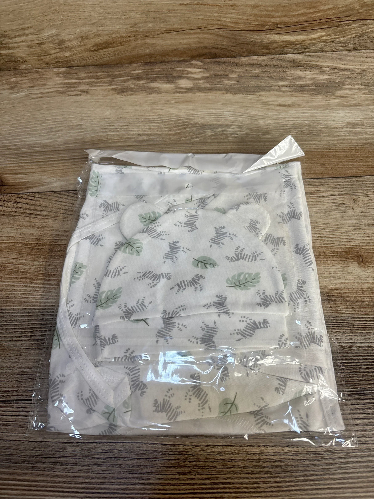 Top-down view of newborn swaddle wrap and matching hat showcasing green leaf print and ear-shaped detail on wooden surface