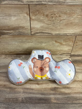 Front view of Taf Toys tummy time support pillow showing printed bear face and two side bolsters on wood floor background