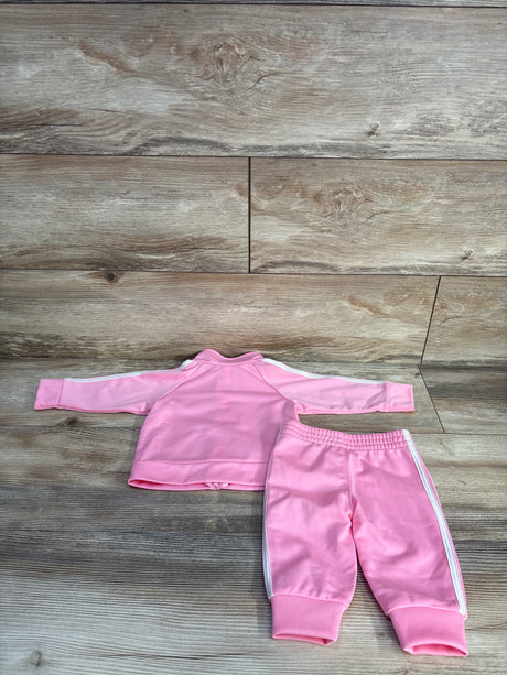 Flat-lay of baby pink Adidas 2-piece tracksuit showing jacket back with white three stripes and matching pants with elastic waist on wood background