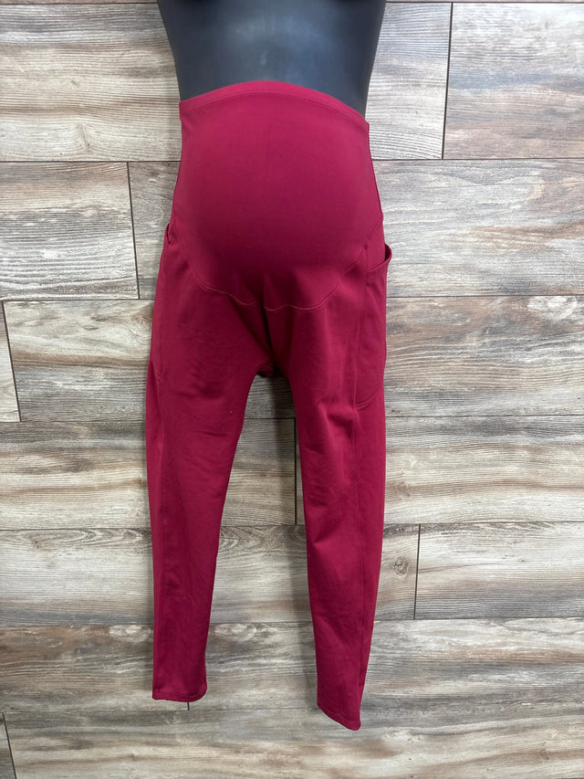 Front view of red maternity leggings on mannequin showing belly panel and side pockets against wood background