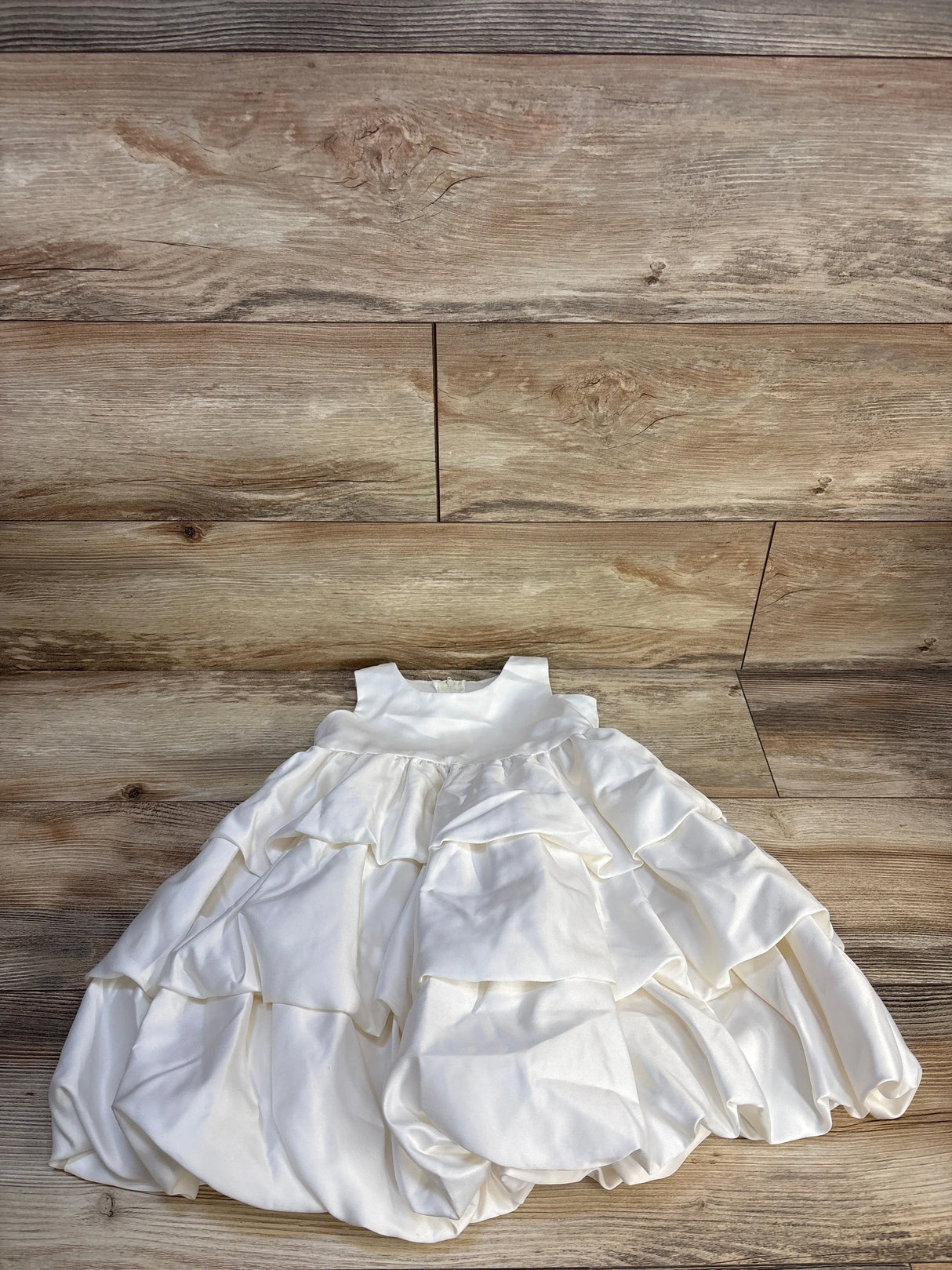 White ruffled baby dress with sleeveless bodice displayed on wood background