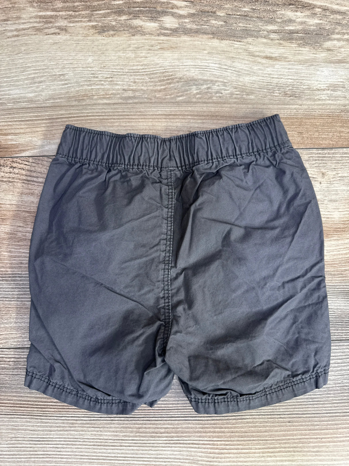 Back view of Old Navy grey toddler drawstring shorts showing elastic waistband and gathered leg hems on wood background