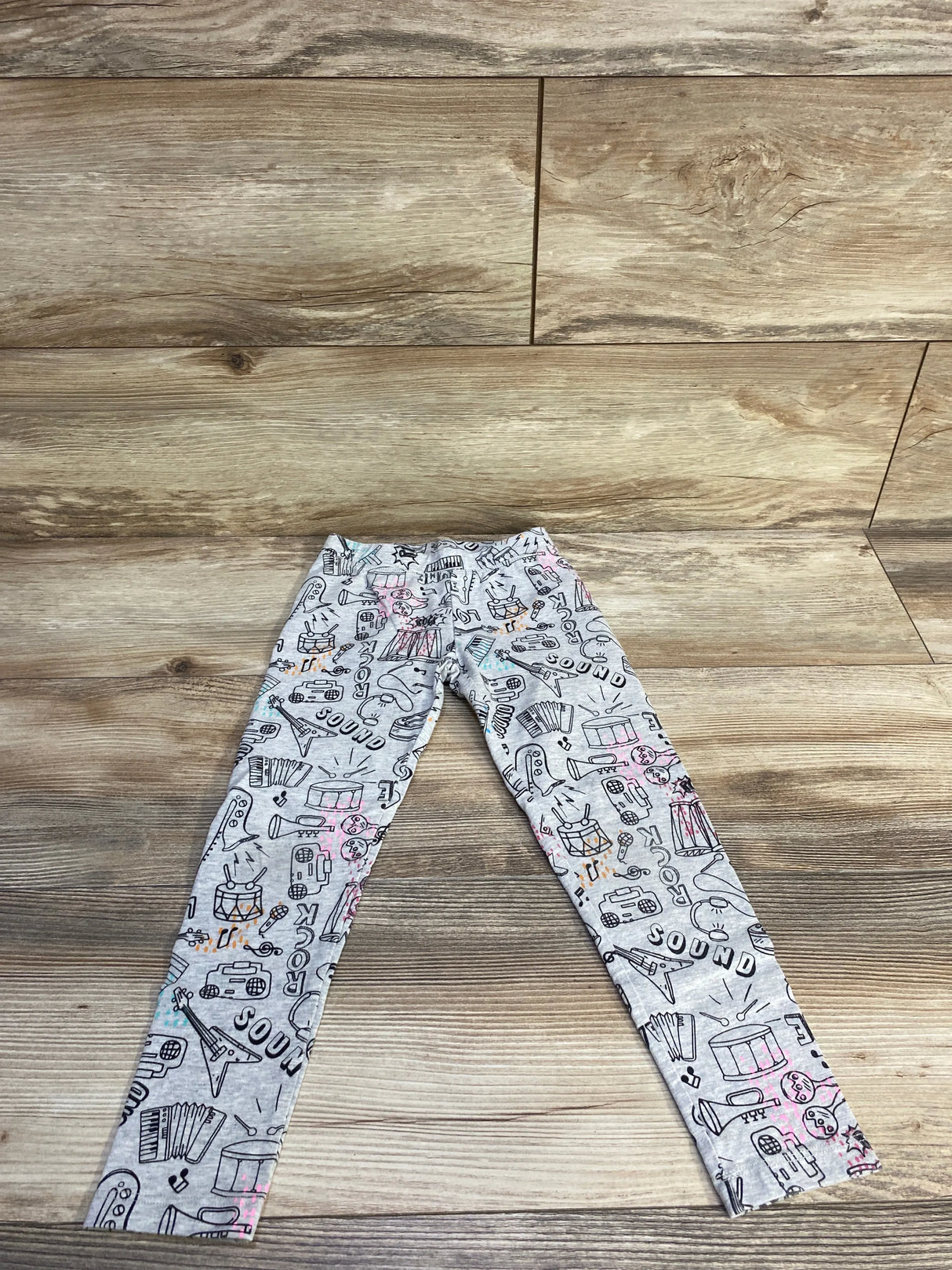 Flat lay of grey Spotted Zebra Rock leggings showing all-over music and instrument doodle print with pink and teal accents on wood background