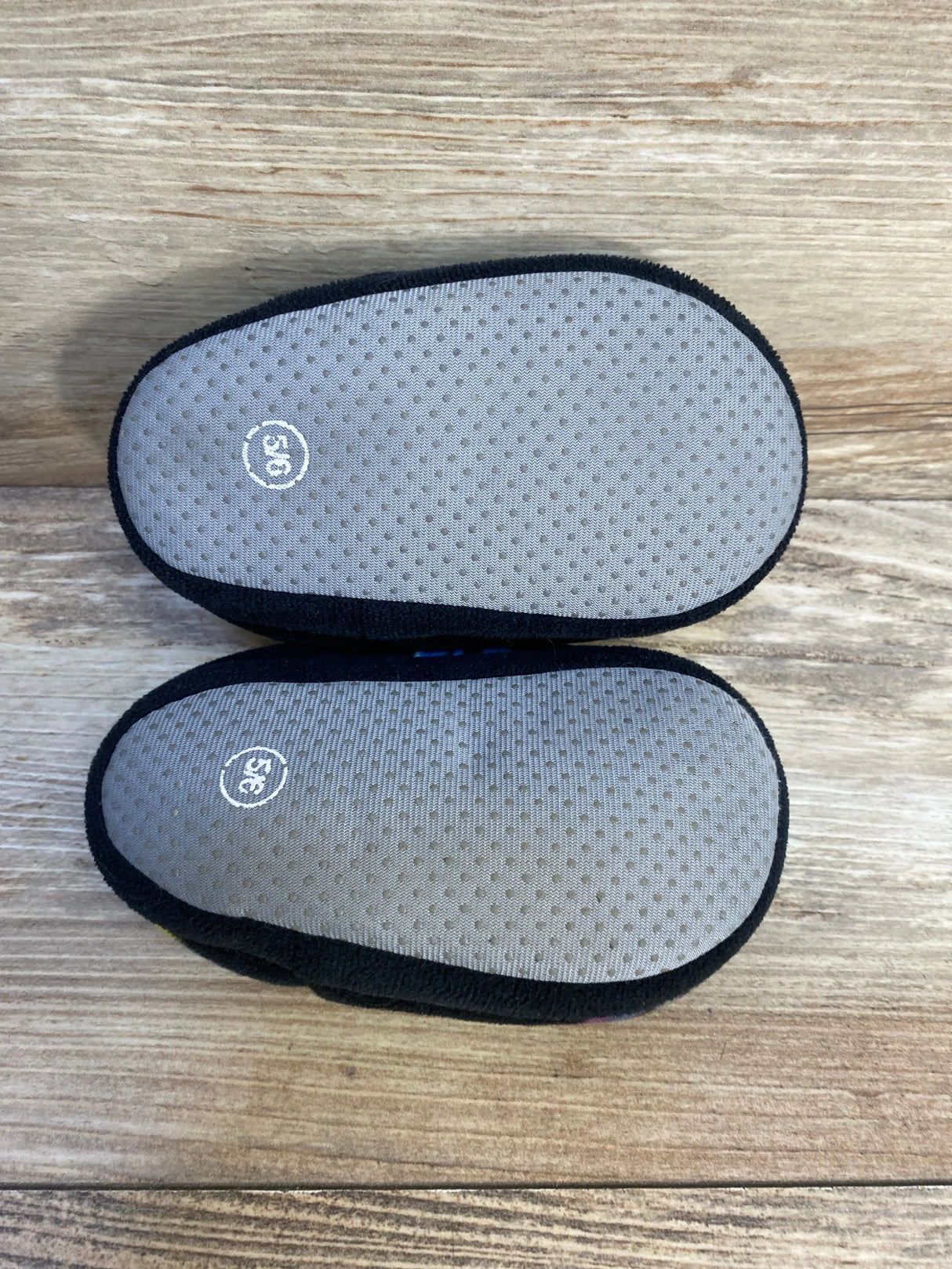 Pair of black baby shoes size 5C with non-slip gray soles on wood background