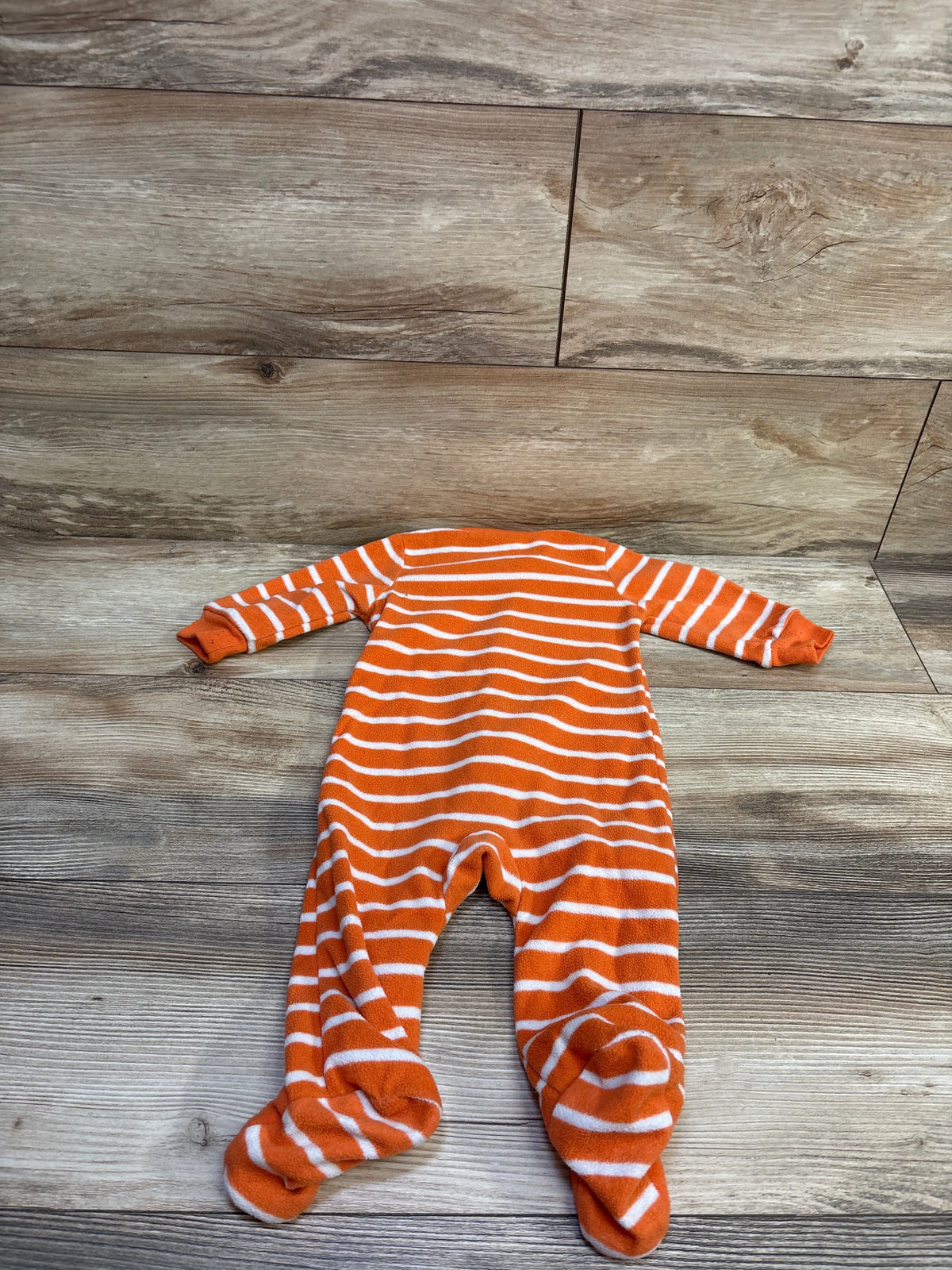 Top view of the striped pumpkin blanket sleeper in orange, showing long sleeves and footed legs on wood-look flooring
