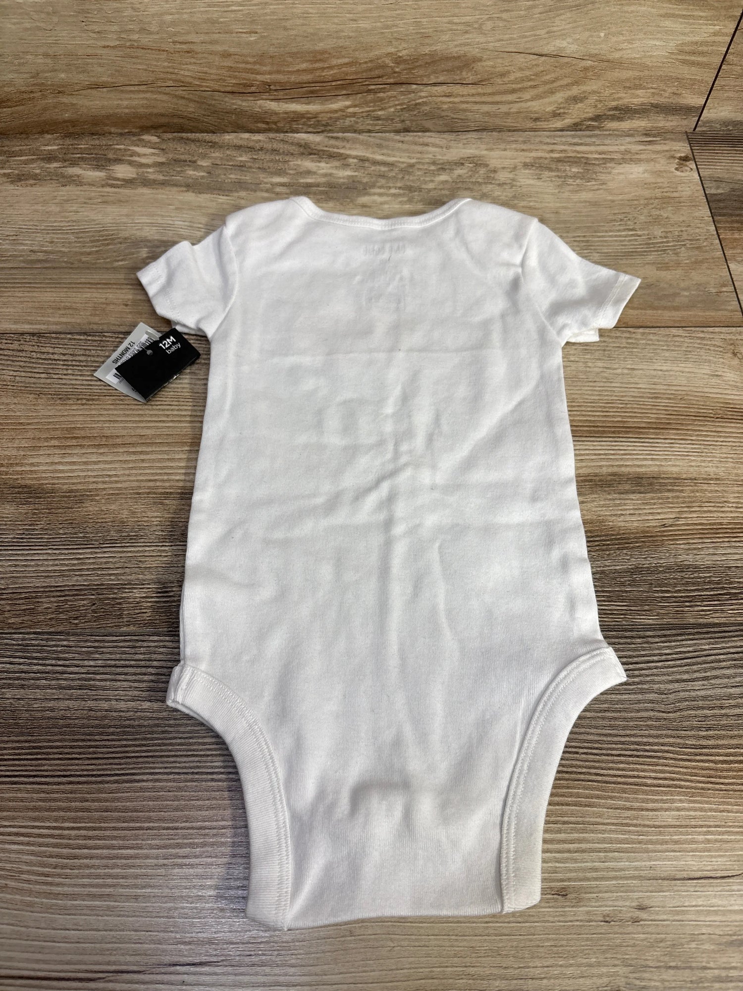White baby onesie with tag, size 12M, laid on wooden floor