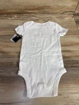 White baby onesie with tag, size 12M, laid on wooden floor