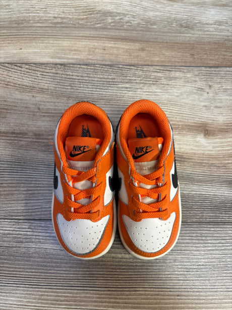 Top-down view of toddler Nike Dunk Low Halloween sneakers, orange and white with black Swoosh, on wood floor