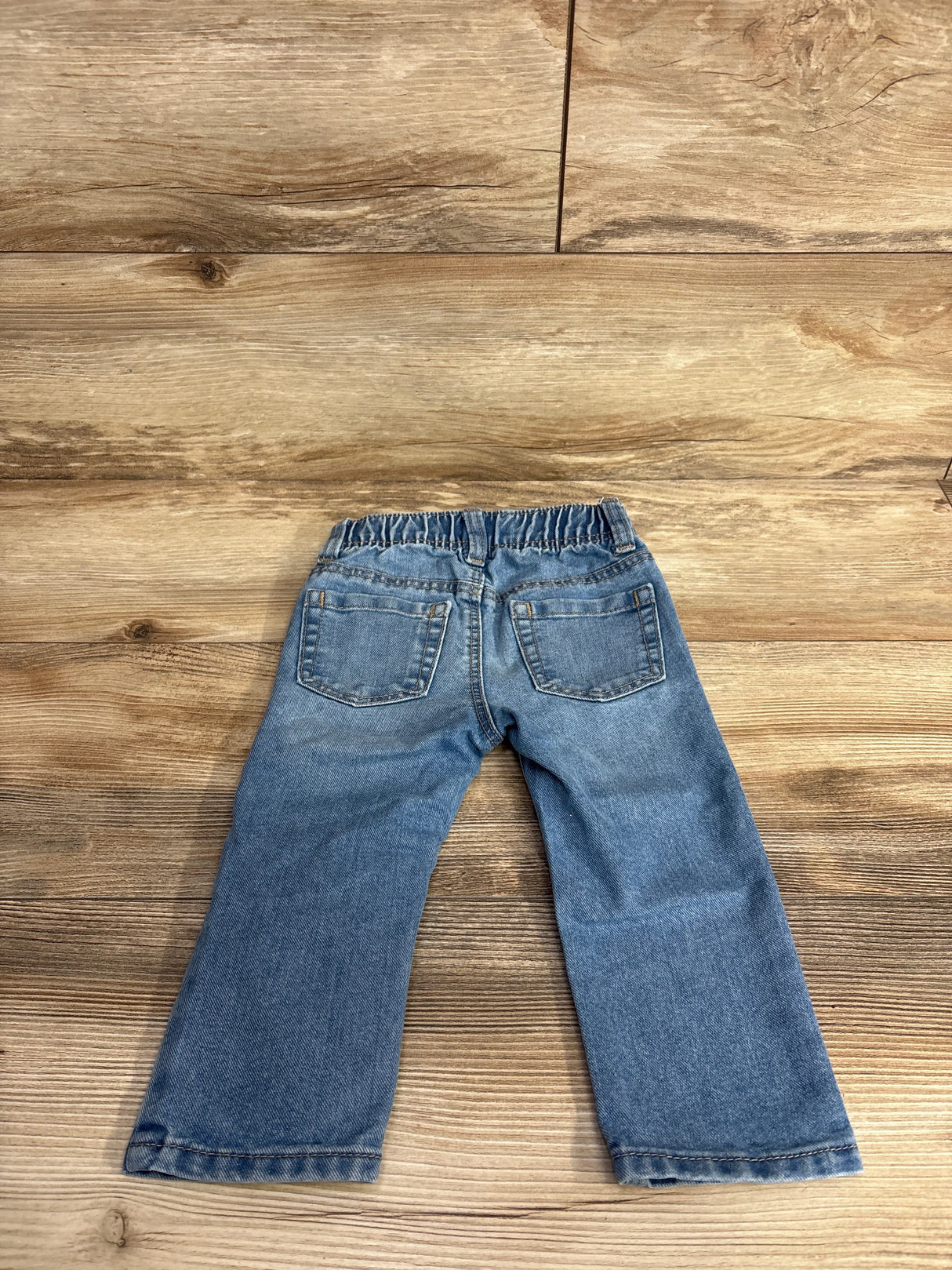 Back view of blue elastic waist toddler jeans laid flat on wood floor for kids clothing resale