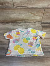 Top view of cream baby short-sleeve shirt with pastel fruit and ice cream motifs on wood background