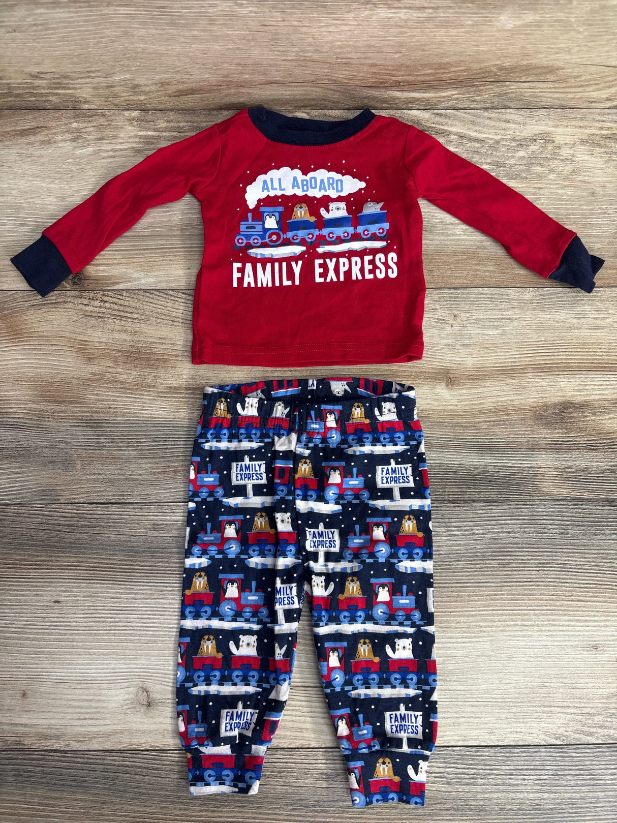 Red long-sleeve toddler shirt with train and animals, matching navy blue train-print pants on wood floor