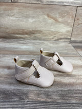 Three-quarter view of beige soft-sole baby shoes with scalloped T-strap and pebbled leather on light wood background