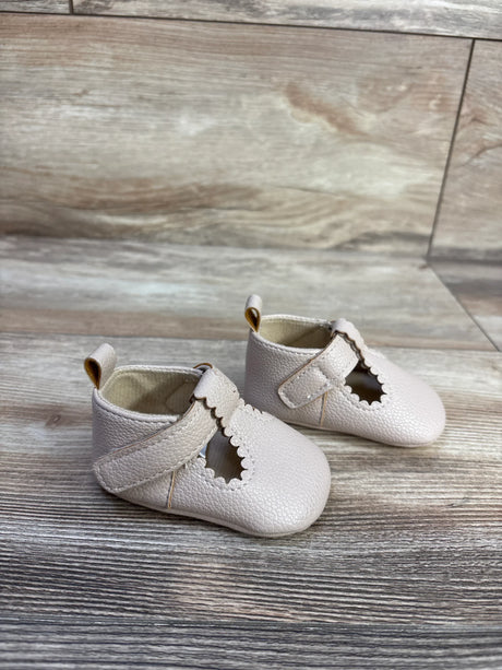 Three-quarter view of beige soft-sole baby shoes with scalloped T-strap and pebbled leather on light wood background