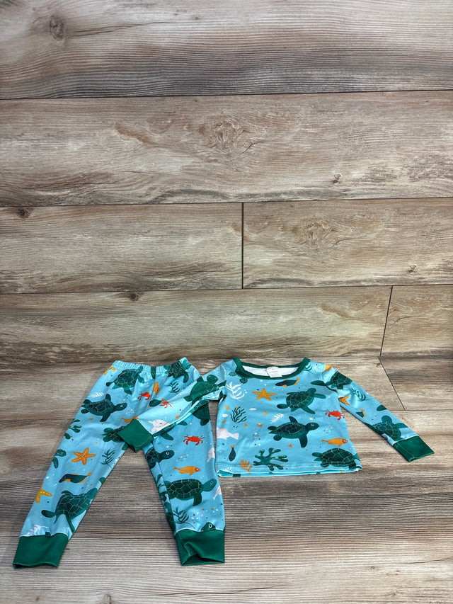 Flat-lay toddler 2-piece blue sea turtle pajama set with all-over sea-life print and green cuffs on wood background
