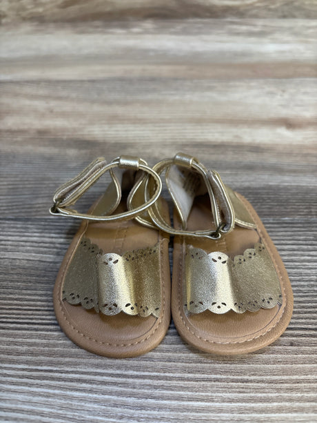 Gold baby sandals with scalloped straps on wood background
